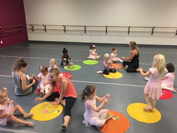 A group of children are sitting on the floor in a dance studio.