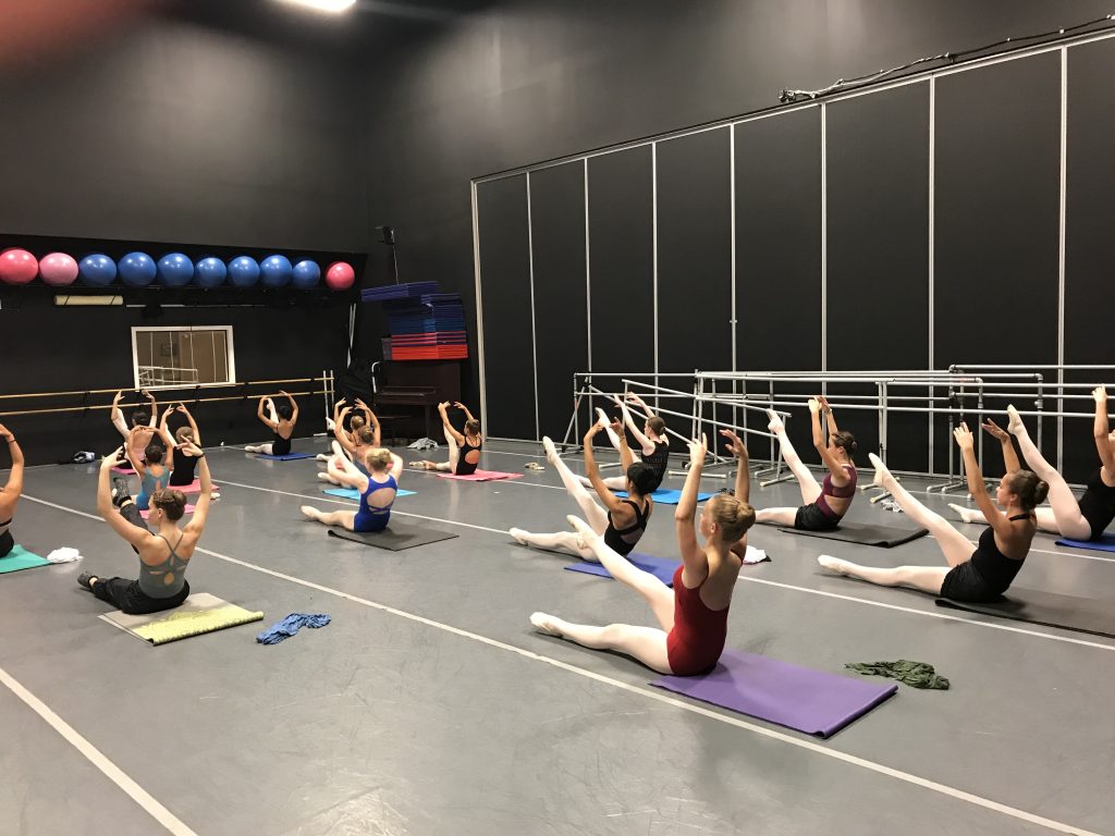 A group of dancers doing yoga in a dance studio.