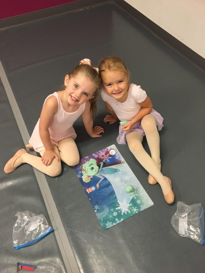 Two little girls sitting on the floor with a picture of a mermaid.