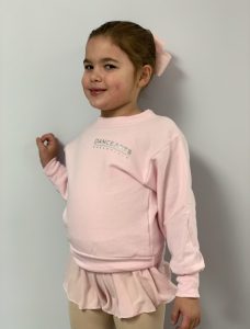 A little girl wearing a pink sweatshirt and skirt.