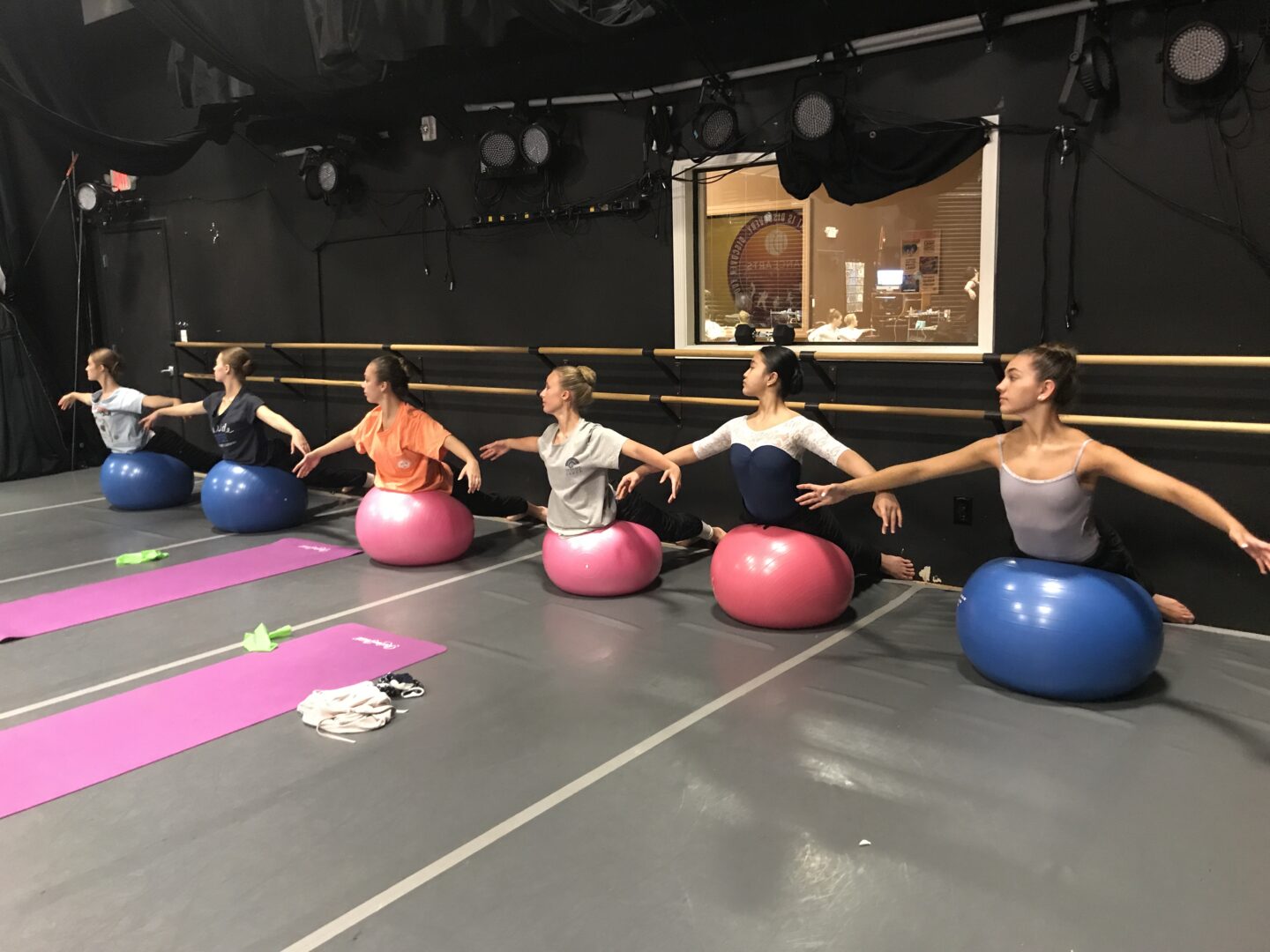 A group of dancers in a studio doing yoga on exercise balls.